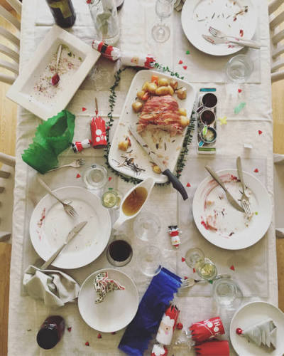 A long table seen from above at the end of a feast β loaded plates, bread and meat, wine, the meal nearly done.