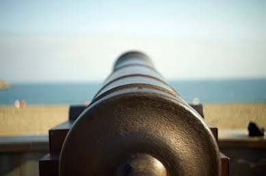 A bronze cannon on a shoreline fortification, pointing out over the sea β a bronze wall guarding the coast.